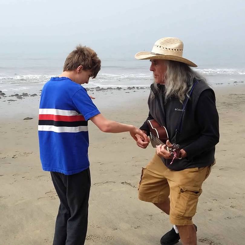 A student playing a guitar with a community member at the beach